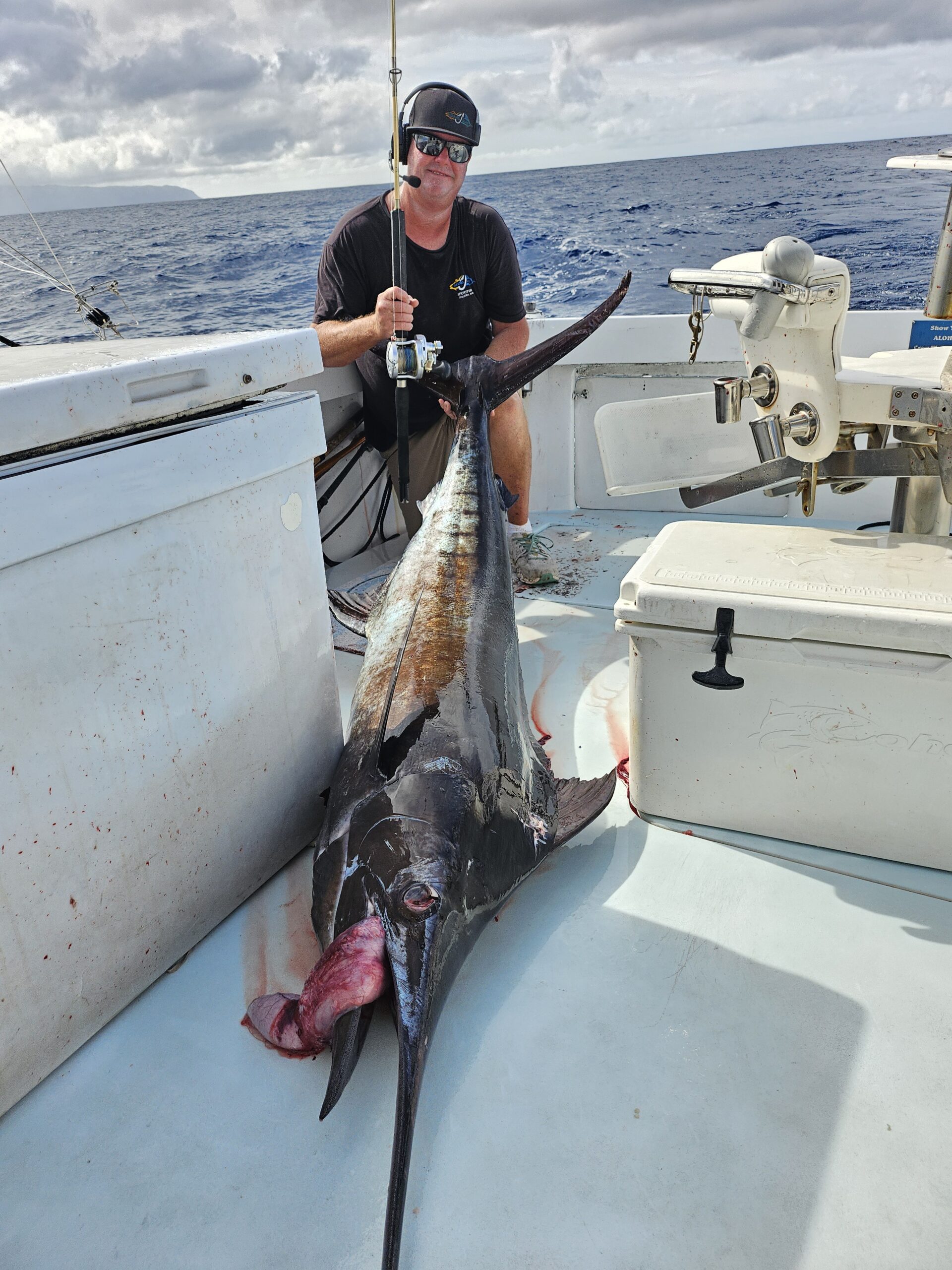 A man proudly displays a large caught shark on a boat.