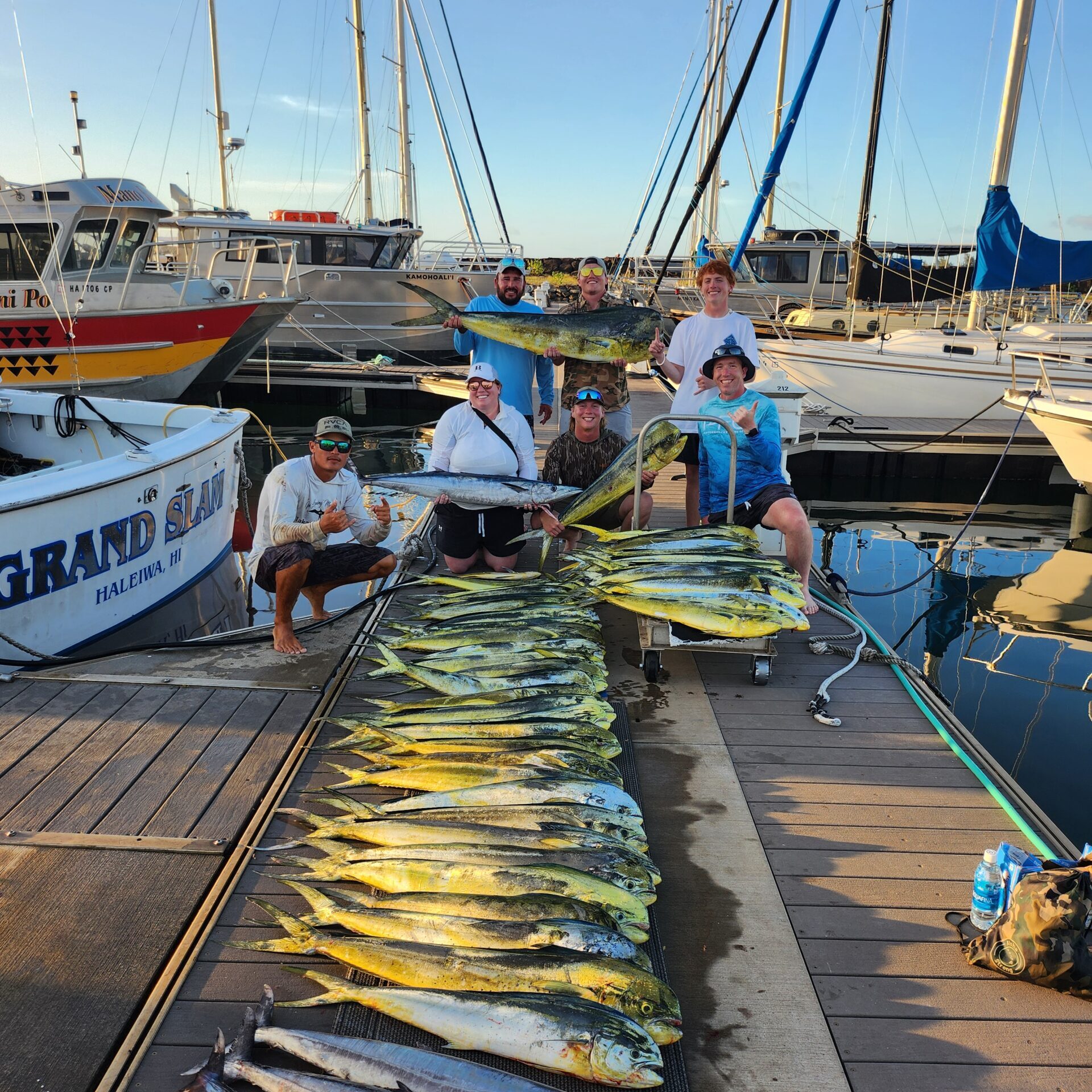 Fishermen proudly display their large catch of fish on a dock at sunset.